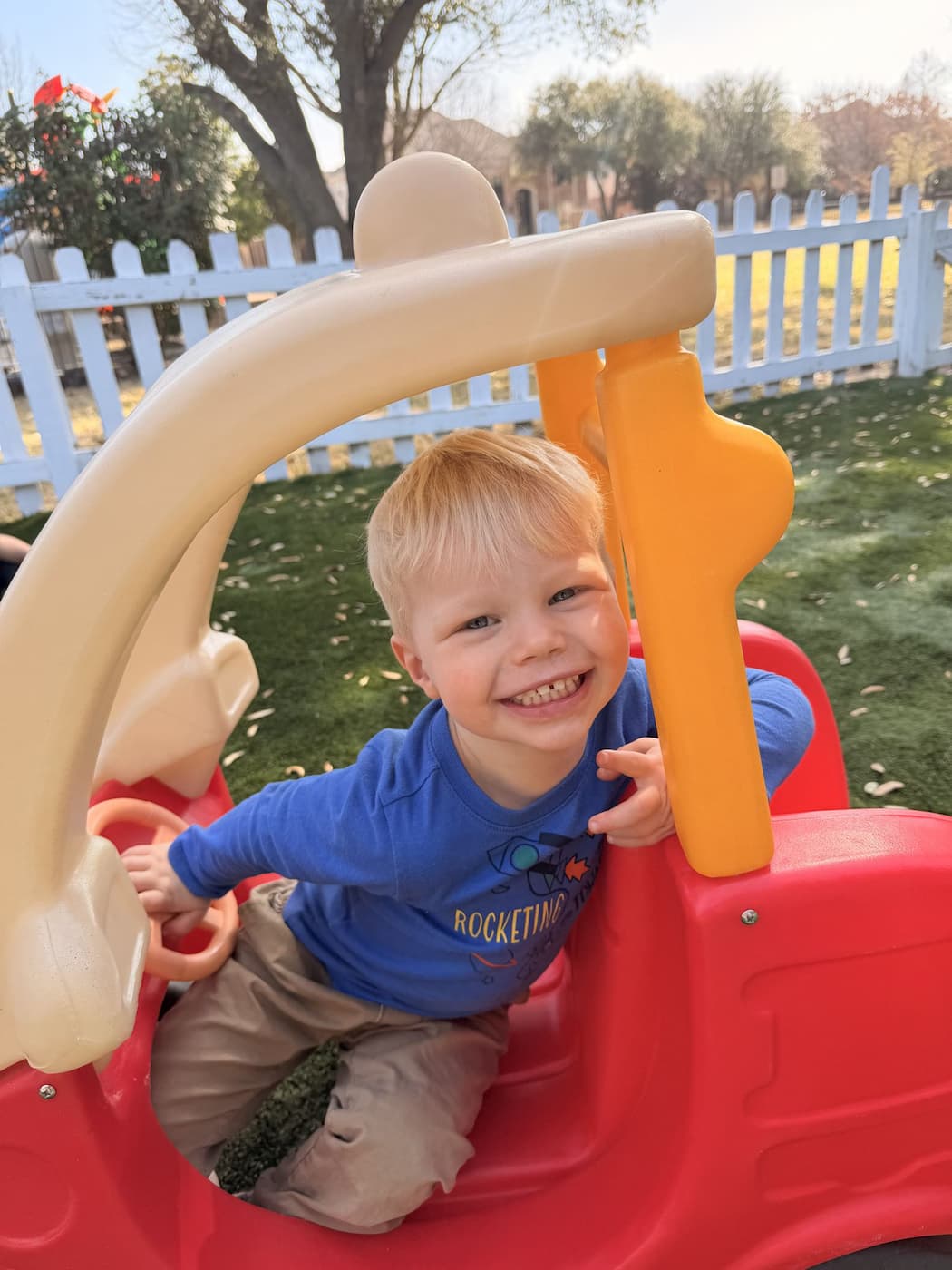 Child smiling in toy car during safe outdoor campus play at Palm Grove Montessori Plano